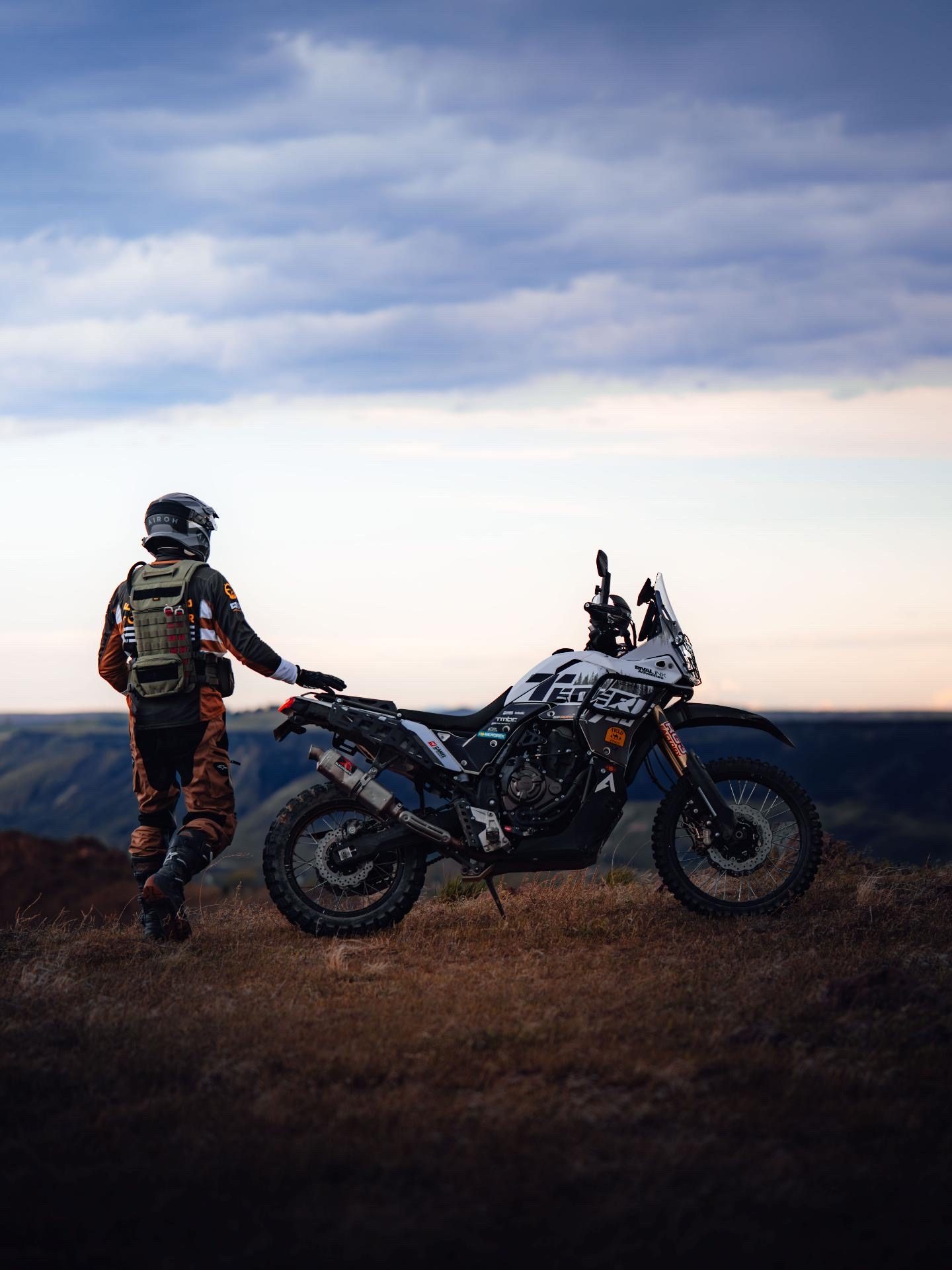 Rider standing beside the Ténéré at a canyon overlook at dusk