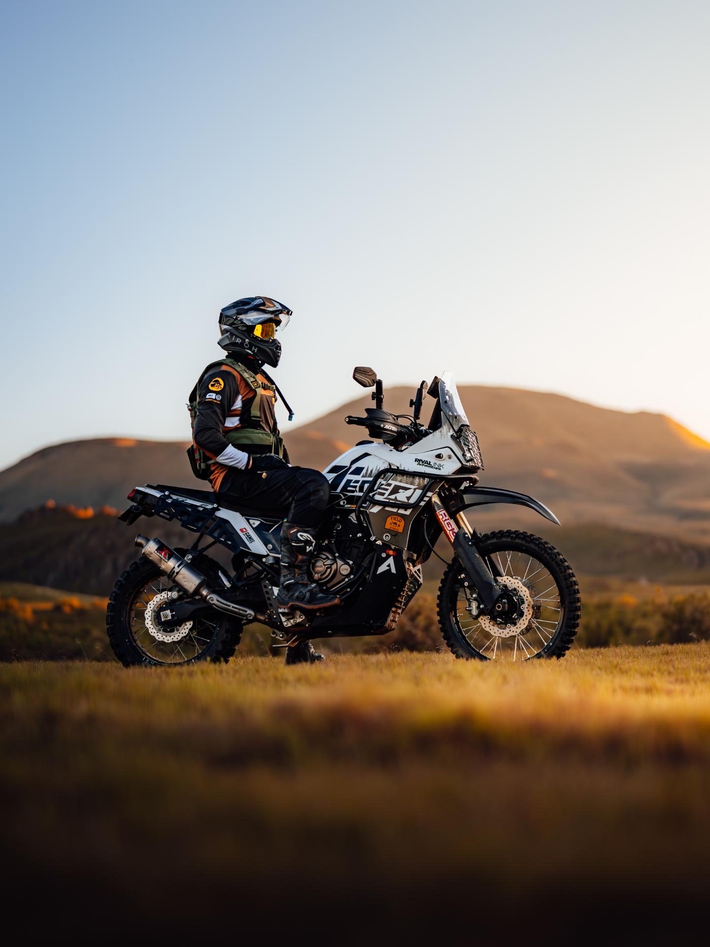 Rider seated on the Ténéré in profile, mountains backlit at golden hour